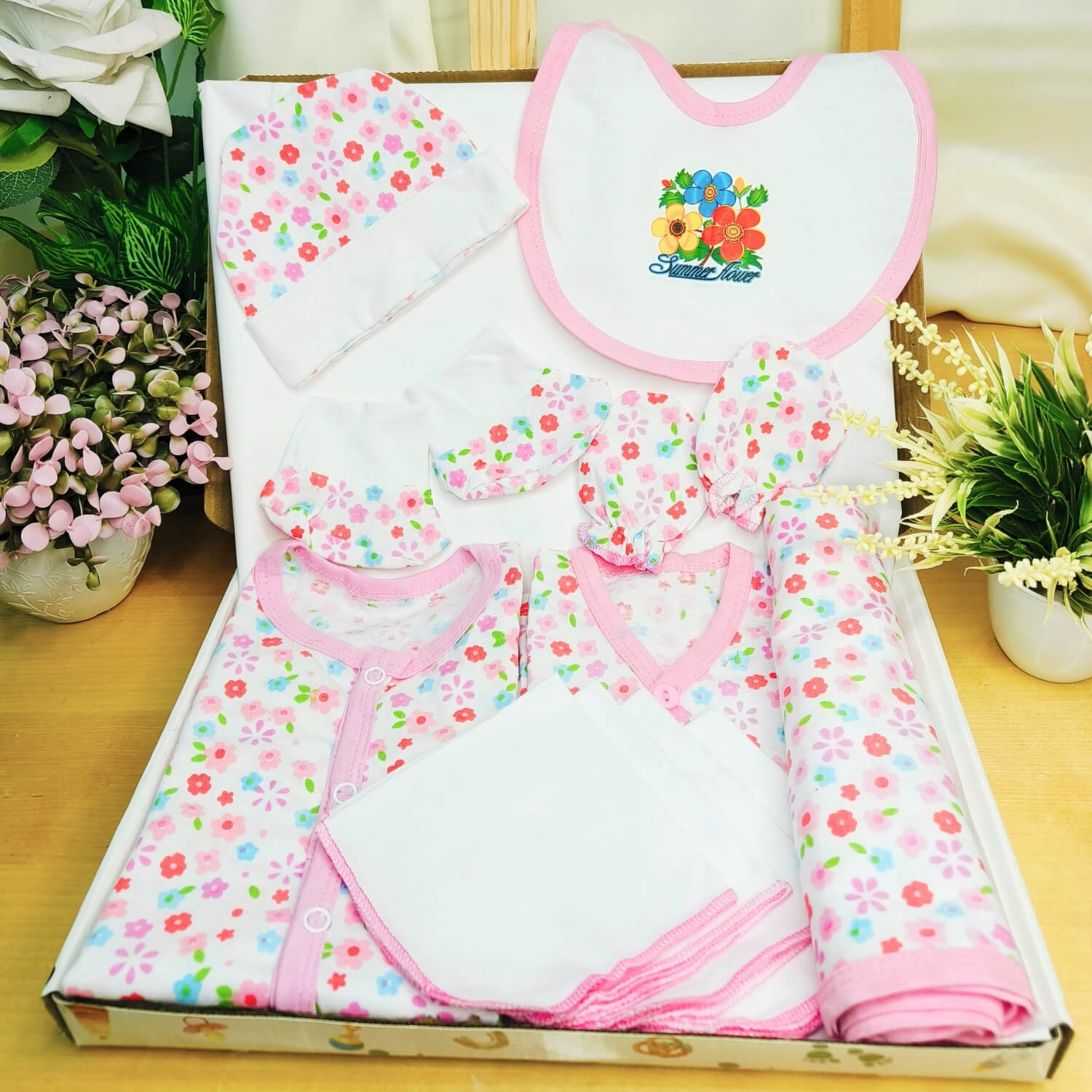Cutetales Baby clothing set with floral patterns on a box, surrounded by plants.