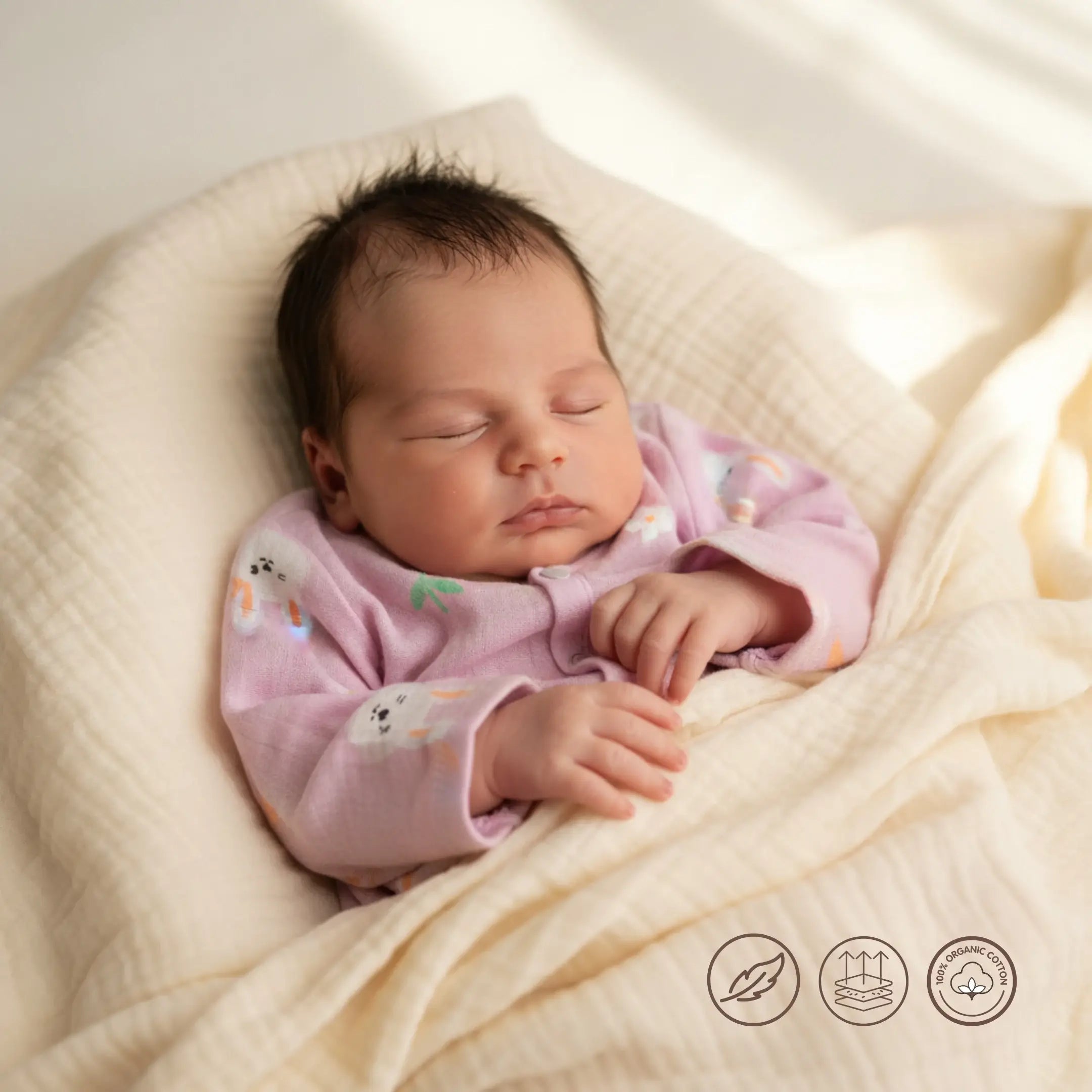 Newborn baby in a pink outfit lying on a soft beige blanket with certification logos at the bottom.