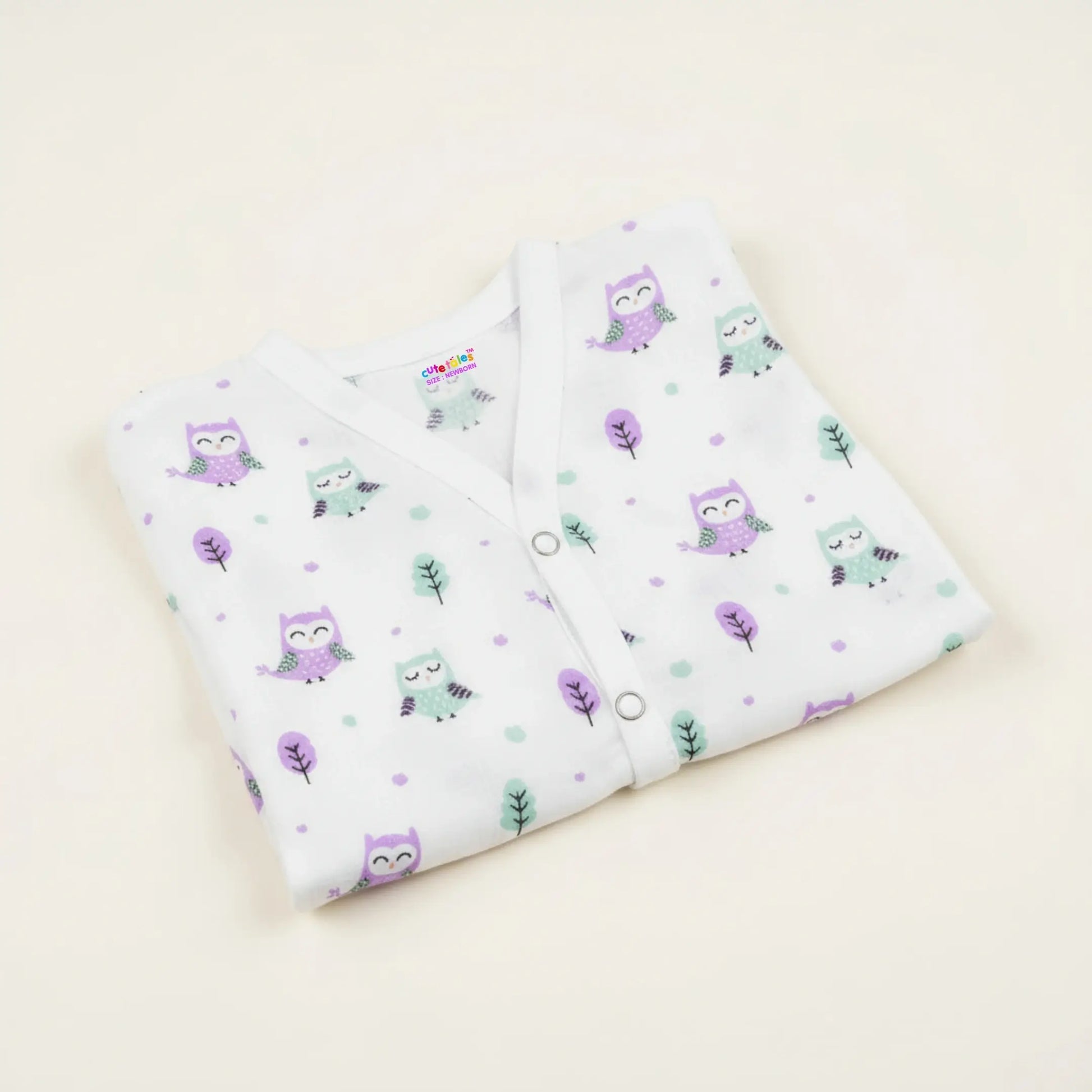 Folded baby outfit with owl pattern on a light beige background