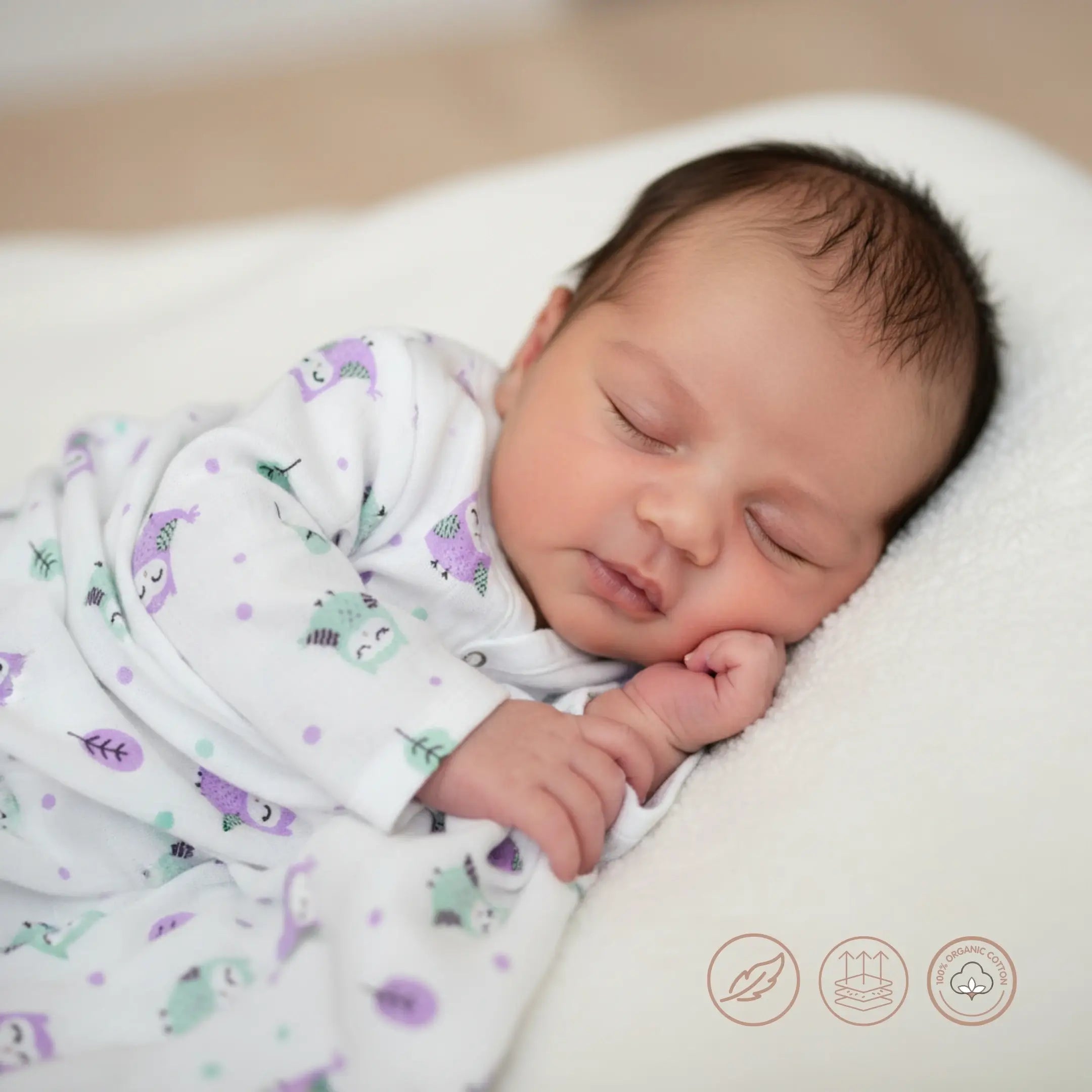Newborn baby sleeping peacefully wrapped in a patterned blanket on a soft surface.