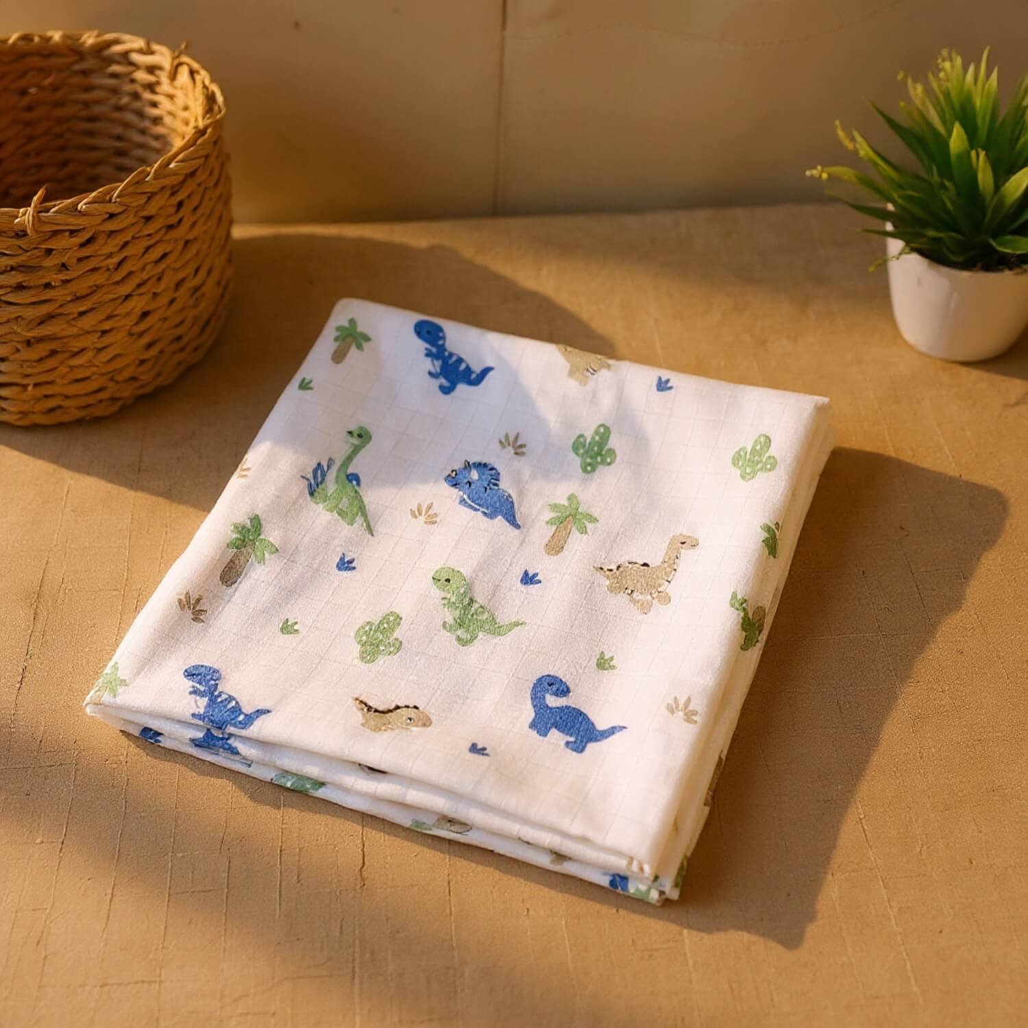 Cutetales Folded fabric with dinosaur pattern on a wooden surface with a basket and plant in the background